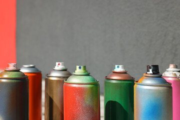 Cans of different spray paints near wall outdoors, closeup