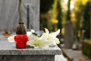 White lilies and grave lantern on granite tombstone outdoors, space for text. Funeral ceremony