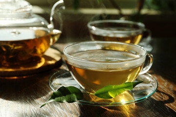 Fresh green tea in glass cups with saucers, leaves and teapot on wooden table