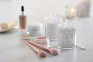 Cotton buds and pads in transparent holders near makeup brushes on table indoors