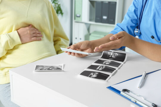 Doctor showing ultrasound picture to pregnant woman in clinic, closeup