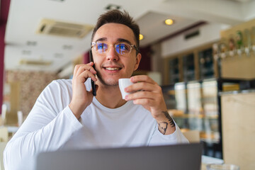 A young businessman in cafe using his laptop mobile phone and wireless earbuds while working on his project business on his laptop and talking on the phone 