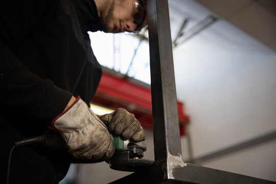 A worker uses a sander on a metal bar in a workshop.