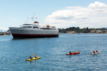 Kayakers passing a ferry near the ocean.