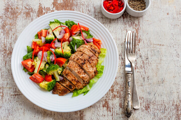 Healthy food grilled chicken vegetable salad in plate on white wood background.