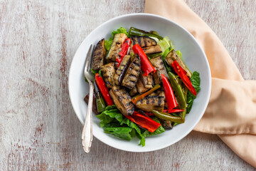 Healthy food eggplant salad has bell pepper romaine in bowl on white wood table.