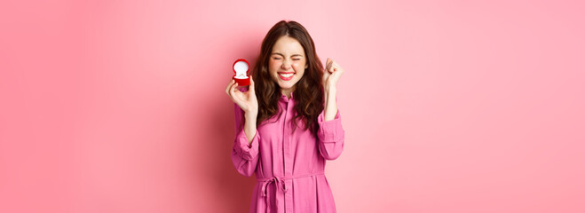 Excited young woman showing engagement ring and celebrating getting married, smiling happy, talking...