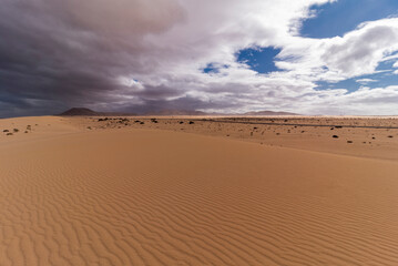 Sand dunes, nature reserve with highway and volcanic scenery in distance during cloudy and rainy day, Canary Islands, Fuerteventura 