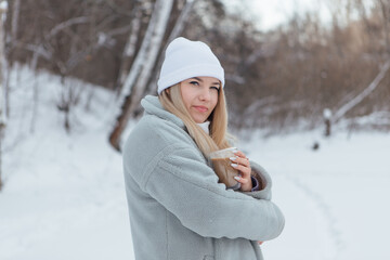 A beautiful young girl smiling and enjoying drinking coffee in a winter forest.