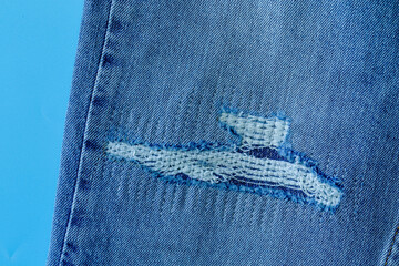 Hole on Denim Jeans. Ripped Destroyed Torn Blue jeans background. Close up blue denim jean texture