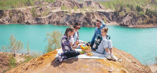 Panorama of young family on picnic after hiking in mountains. Beautiful view of blue lake