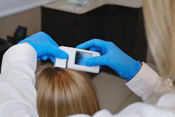 Naklejka premium Close up view of the female trihologist examines head skin of woman with special dermatology equipment system. Hairloss and trichology concept
