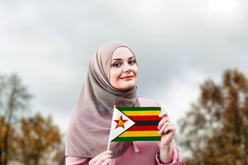 Muslim woman in hijab holds flag of Zimbabwe
 - obrazy, fototapety, plakaty