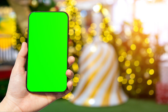 Close-up of female use smartphone blurred images with Colorful balls on Green Christmas tree background Decoration During Christmas and New Year,Green screen