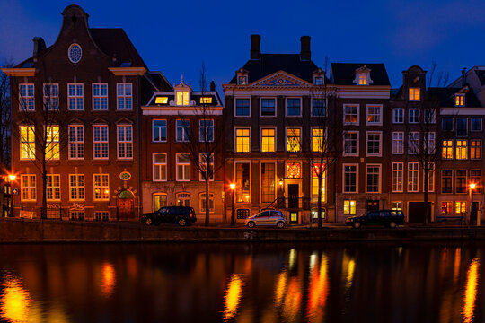 Romantic nocturnal view of Amsterdam: canal in the Red District. Buildings, cars and boats are reflected in the water