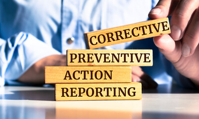 Wooden blocks with words 'Corrective Preventive Action Reporting'.