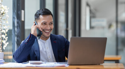 Obraz premium Young business Asian man working at workplace with laptop and papers on desk and using phone.