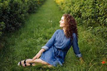 Fototapeta premium Happy young woman with brown curly hair, wearing a dress, posing outdoors in a garden