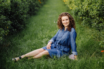 Fototapeta premium Happy young woman with brown curly hair, wearing a dress, posing outdoors in a garden