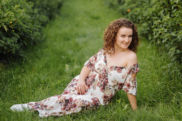 Happy young woman with brown curly hair, wearing a dress, posing outdoors in a garden