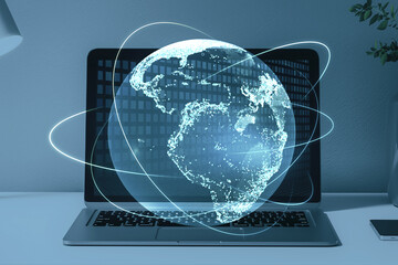 Close up of laptop computer on desktop with creative glowing globe hologram on blurry background. Technology, metaverse and digital map concept. Double exposure.