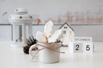 New Year and Christmas atmosphere, December 25 on the calendar. Cup with drink and marshmallow, tree house behind