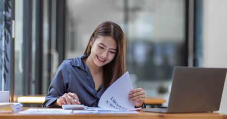 Asian Businesswoman Using laptop computer and working at office with calculator document on desk, doing planning analyzing the financial report, business plan investment, finance analysis concept.
