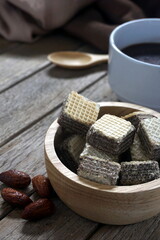 Milk chocolate wafers in wooden bowl and coffee Almonds on the wooden floor