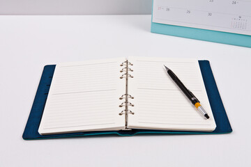 A pen is placed on a diary of blank notes, against the background. You can change the background to any image you want.