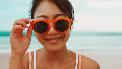 Playful asian woman in orange sunglasses looking to camera.