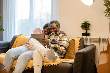 Happy senior African American couple sitting on the sofa controlling their home automation system from the tablet