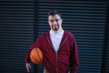 Portrait of young man with down syndrom holding basketball ball.