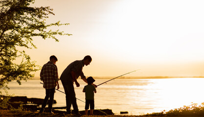 Family dad and two sons are fishing at sunset, silhouette of a man and two boys. - obrazy, fototapety, plakaty