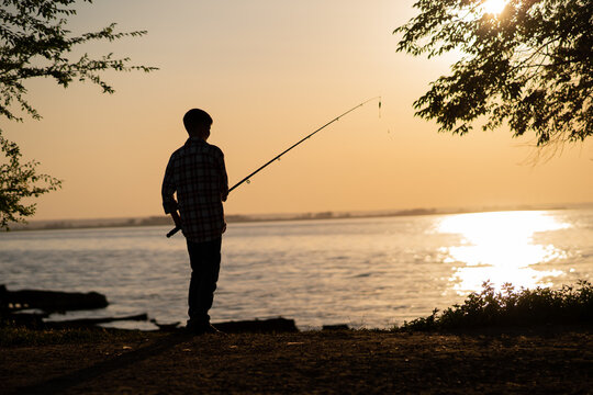 Silhouette of a boy fishing on a lake in the summer at sunset