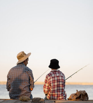 Father and Son together fishing at sunset time in summer day under beautiful sky on the lake.