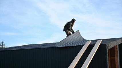 Male builder installing black corrugated iron sheet used as facade of future cottage. Man worker building wooden frame house. Carpentry and construction concept. - Powered by Adobe