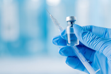 Doctor's hand holding glass vial and syringe with injection over blue background. Vaccination or...