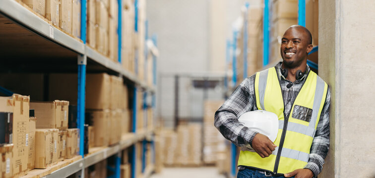 Happy warehouse picker looking away with a smile, man stands in a logistics centre with a voice picking headset and a helmet