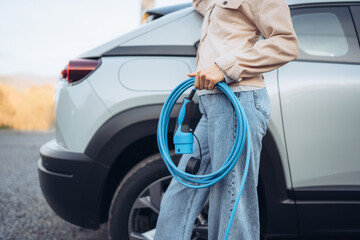 Close-up of woman holding power supply cable from her electric car, prepared for charging it in...