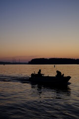 夕暮れ時に川で小舟に乗って釣りをする人