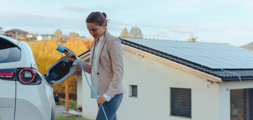 Young woman charging her electric car in home, sustainable and economic transportation concept.