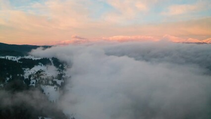 Drone flight among beautiful low clouds and mists creeping over the snow-covered mountain slopes, the Rhodopes in Bulgaria at winter sunrise. - Powered by Adobe