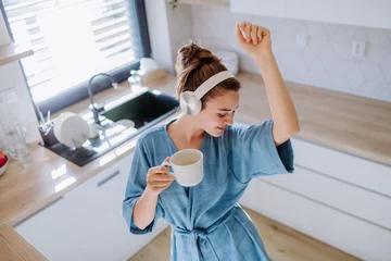 Fotobehang Young woman listening music and enjoying cup of coffee at morning, in her kitchen. © Halfpoint