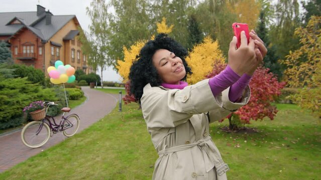 Beautiful woman taking a selfie photo with her smartphone outdoors. Cheerful, pretty girl in her 30s using her smartphone to take pictures with colorful foliage behind. High quality 4k footage