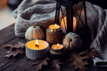 Cozy autumn composition with aromatic candle, pumpkins, wool sweater, leaves, cinnamon. Aromatherapy on a grey fall morning, home atmosphere of cosiness and relax. Wooden background close up.