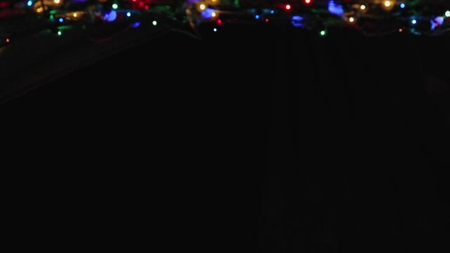 Glowing Christmas garland at the top of the frame on a black background. Place to copy. New Year multi-colored lights in defocus. Beautiful holiday card, video for intro, text, intro. UHD 4K.