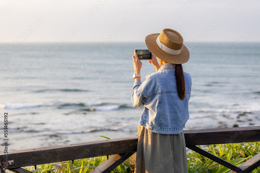 Poster travel woman use cellphone to take photo at seaside under sunset period