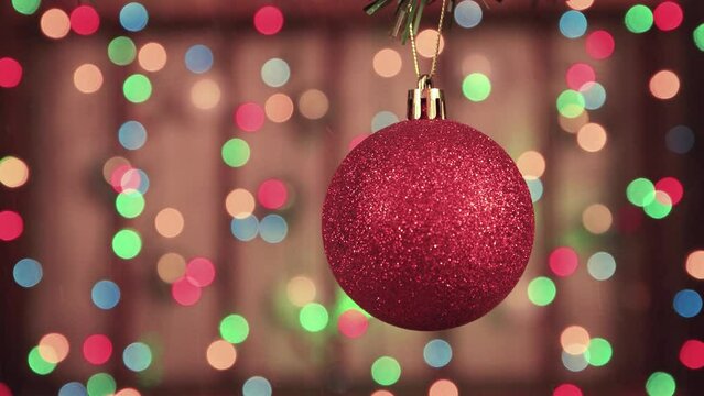 New Year's burgundy ball hangs against the background of glowing lights. Christmas colorful garlands out of focus. Holiday card with bokeh. Abstract background for captions and text. UHD 4K.