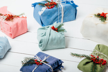 Eco friendly christmas gift packing concept. Gift boxes wrapped in fabric with spruce branch and berries on the white wooden background. No plastic, zero waste holidays. Selective focus.