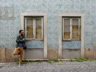 Fototapeta na wymiar A handsome, curly-haired man with a beard and casual dress, in front of the traditional facade of a Portuguese house. Traditional tiles from Portugal